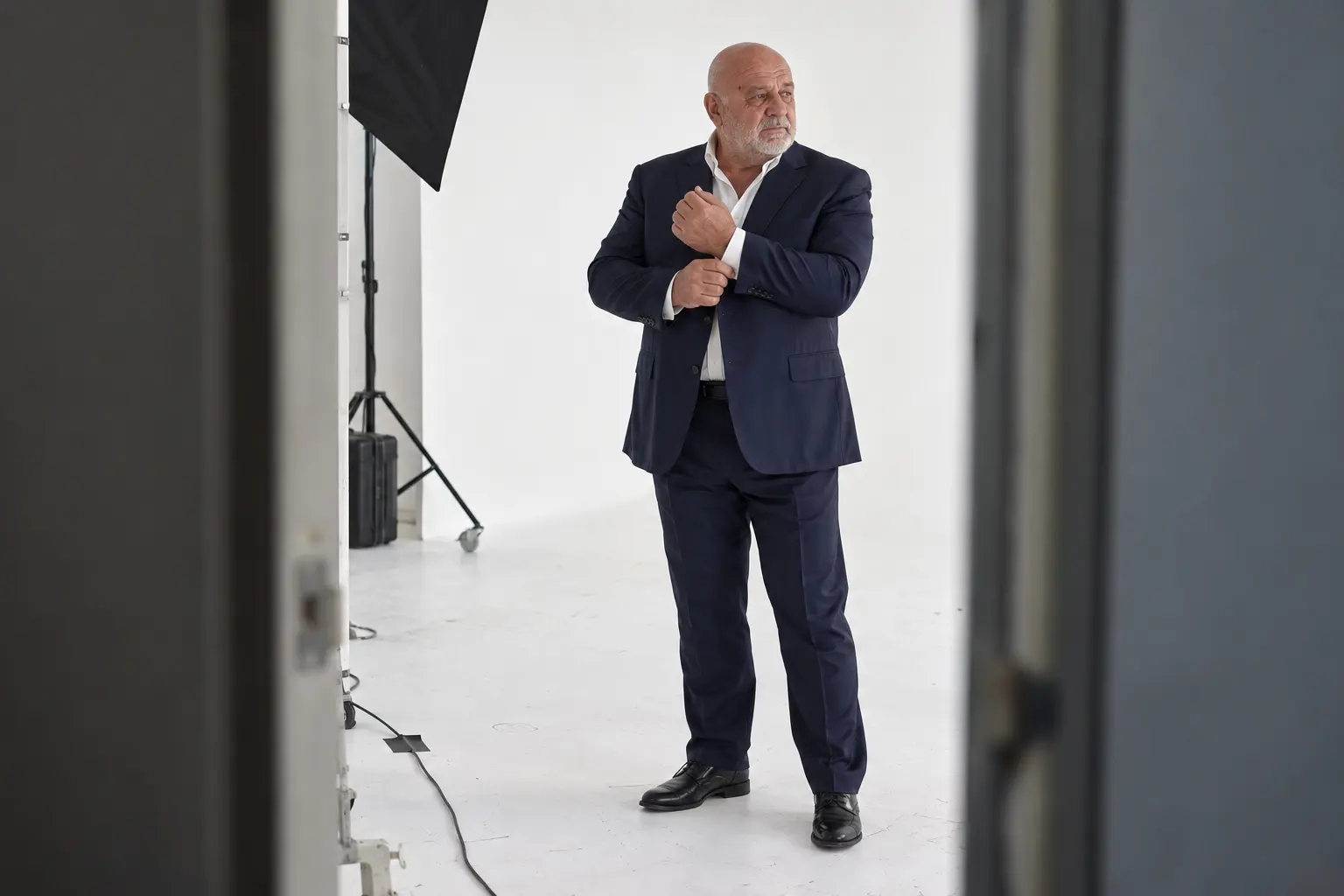 Ankara'daki beyaz fotoğraf stüdyosunda lacivert takım elbiseli, beyaz kirli sakallı erkek model.