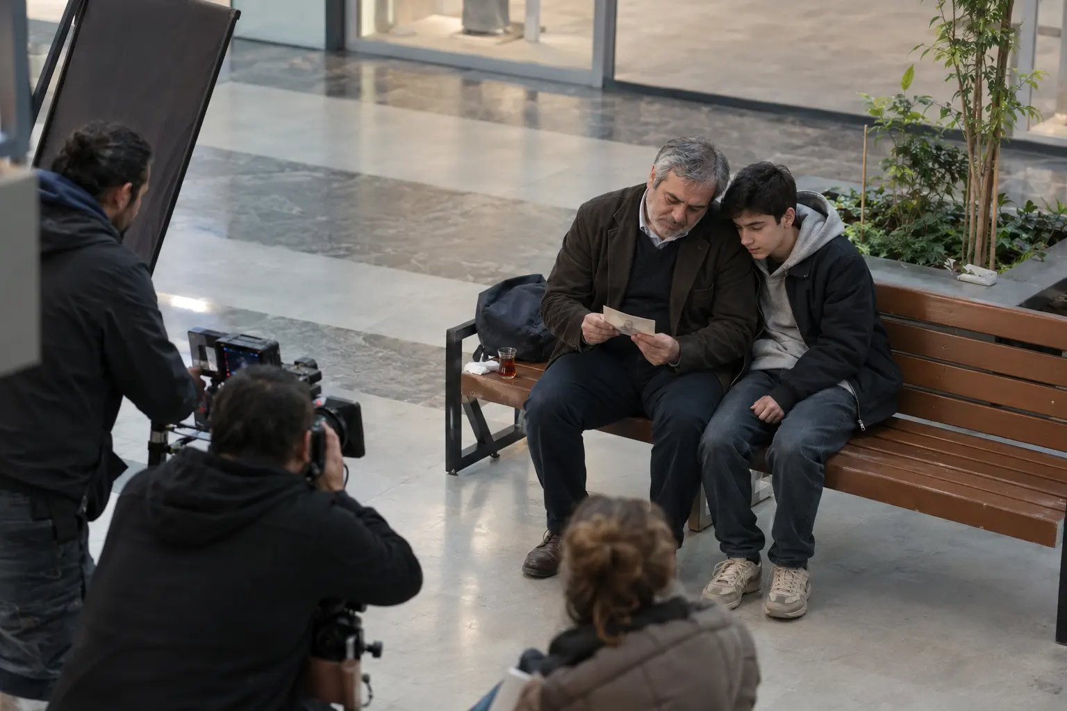 Alışveriş merkezi atriumunda oğluyla eski bir fotoğrafa bakan olgun oyuncunun klip çekimi.